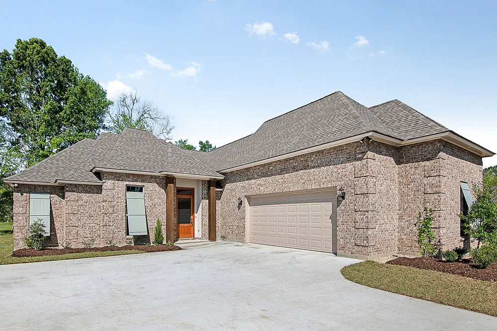 Brick Acadian-style home with a side-entry garage and cedar porch posts