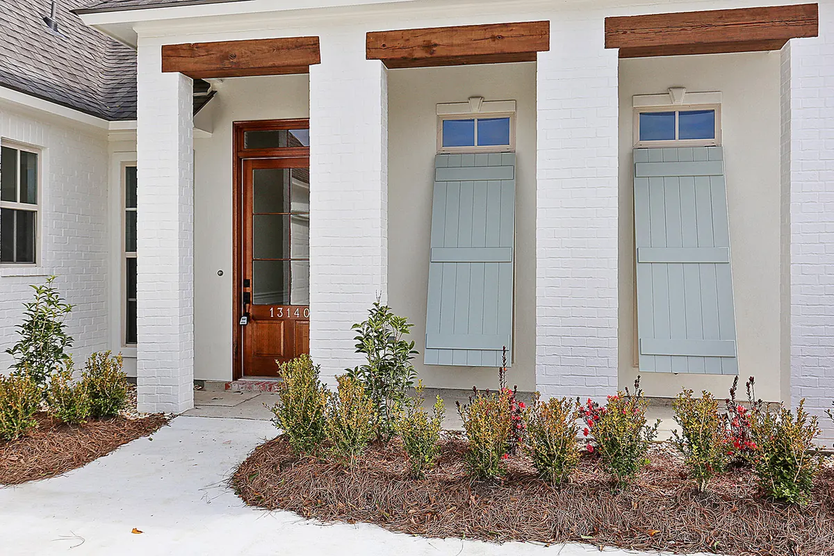 Painted brick porch with rough-sawn cedar beams, a wood front door and blue-gray board shutters