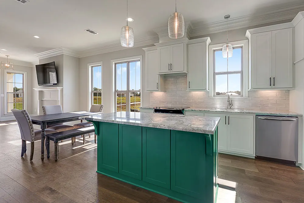 White kitchen with a deep green island and a dining area by tall windows