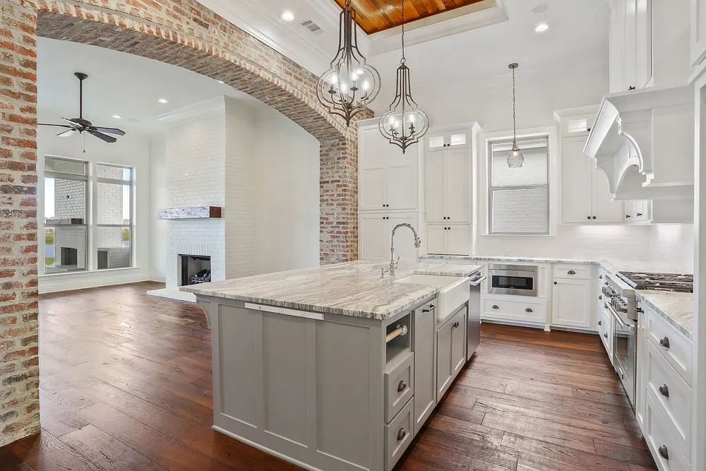 Kitchen and living room joined by an exposed brick arch, with a marble island and pendant lights