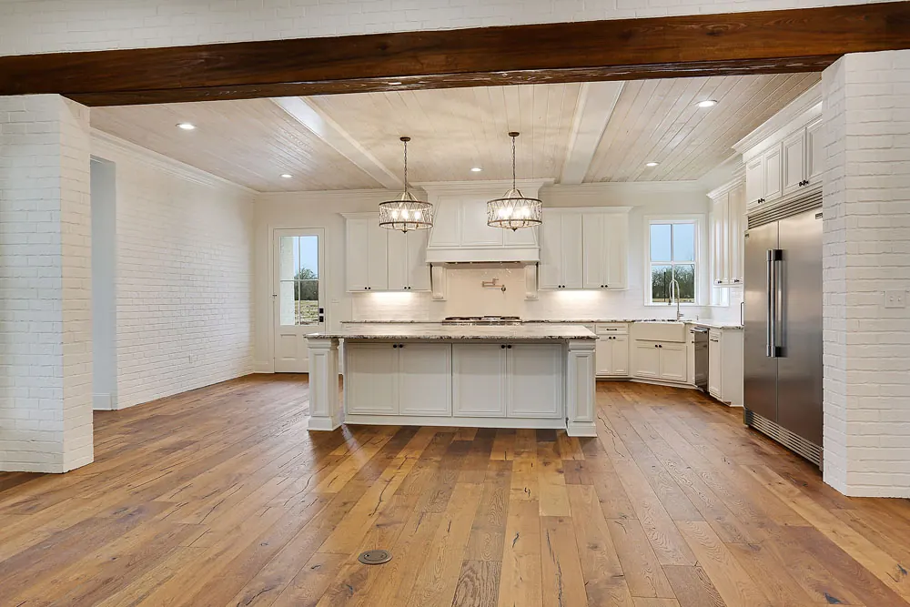 Open kitchen with a large island, a stained wood ceiling beam, white cabinets and wide-plank wood floors